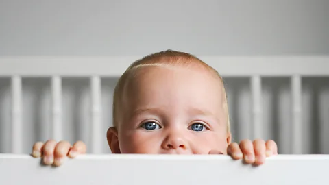 A cheeky infant is standing in a crib (Credit: Getty Images)