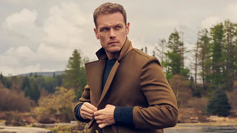 Actor Sam Heughan tightens his coat as he looks into the distance of the Scottish wilderness (Credit: Galloway Distillery Media)