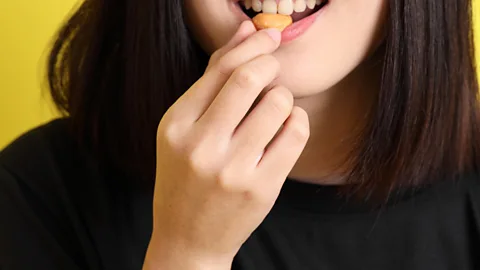 A close up of a woman's mouth as she places a nut between her teeth (Credit: Getty Images)