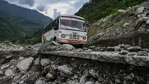 A bus in Nepal picks its way along a road on a hillside that is crumbling away beneath the road (Credit: Getty Images)