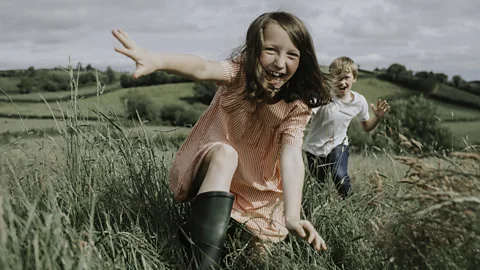 A boy and a girl run joyously through a field (Credit: Getty Images)