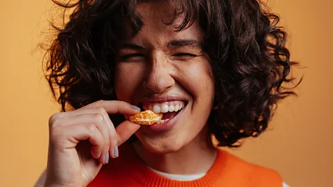 A woman with dark curly hair biting down with enjoyment on an tangerine segment (Credit: Getty Images)