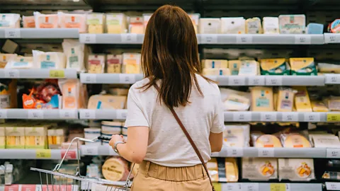 A woman faces away from the camera looking at supermarket shelves of cheese (Credit: Getty Images)