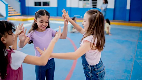 Three young girls playing in circle and pressing their hands together in a school sports hall (Credit: Getty Images)