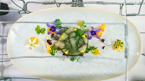 An elegant fish mould on a white plate surrounded by yellow and purple edible flowers (Credit: Courtesy of Sungani Restaurant)
