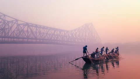Fishermen pull in nets from a small boat at sunrise on the Hooghly River under Kolkata's Howrah Bridge (Credit: Marco Rutten/World Food Photography Awards)