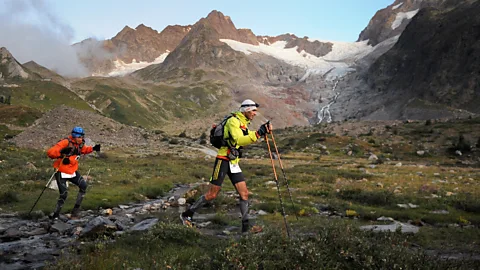 Two trail runners cross an alpine valley beneath a glacier during an ultramarathon in the Alps (Credit: Getty Images)