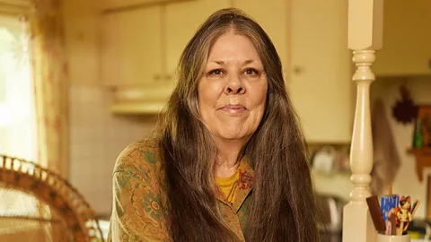 Loreen Willemberg, a woman with long hair, stands in the middle of a warmly lit, homely decorated sitting room (Credit: Ari Michelson/ AUGUST)