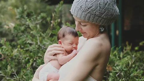 Picture of a woman (Courtney Louise) wearing a hat, out in nature, holding her newborn child against her belly still enlarged from the pregnancy (Credit: Courtney Louise)