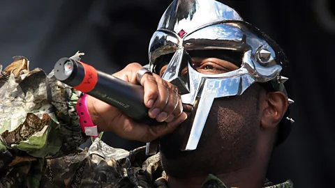 MF Doom rapping into a microphone and wearing a mask (Credit: Getty Images)