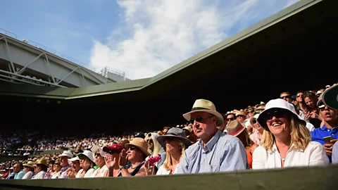 Spectators wearing hats watch a tennis match at Wimbledon beneath a blue summer sky (Credit: Getty Images)