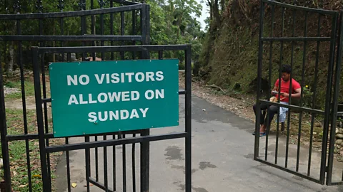 A green sign reading "No visitors allowed on Sunday" hangs on an open gate at the entrance to Mawlynnong, India (Credit: Jamie Fullerton)