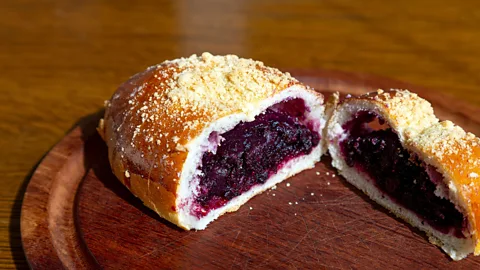 A berry-filled bun cut in two halves on a wooden plate (Credit: Alamy)