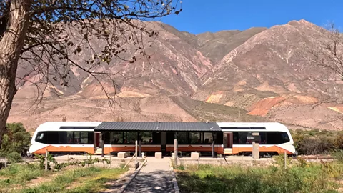 A brown and white solar-powered train stands in front of multicoloured mountains of Argentina's Quebrada de Humahuaca (Credit: Thomas Jowett)