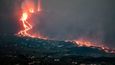 molten lava spills down a hillside towards and past a built up area
