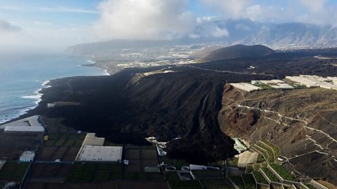 Dried black lava spilled over a hill and covering agricultural fields.
