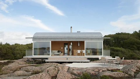 A timber and steel cabin with large sliding glass panels and an outdoor patio, situated on rocky terrain between two fjords in Sweden (Credit: Åke E:son Lindman)