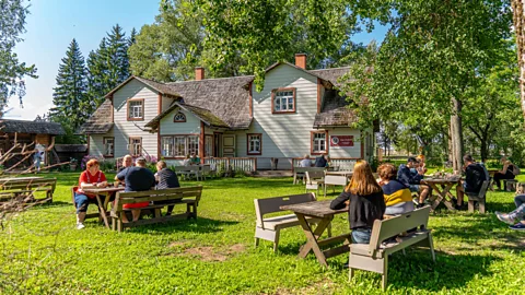 People sitting in a garden at picnic tables with a wooden farmhouse in the background (Credit: Martin Mark)