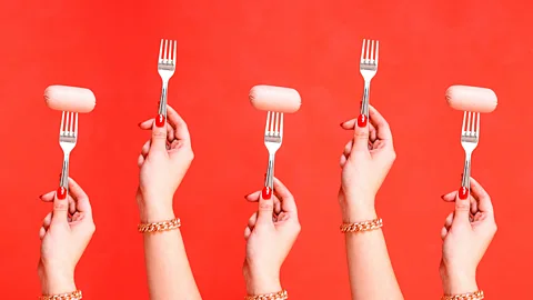 Five hands raise forks to the air, three of them have sausages on them (Credit: BBC/ Javier Hirschfeld/ Getty Images)