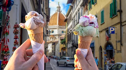 Two ands hold up cones of colourful gelato on the on the streets of Florence, Italy (Credit: Getty Images)