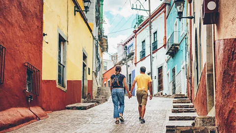 Two people walk hand in hand along a cobbled street lined with colourful buildings (Credit: Getty Images)