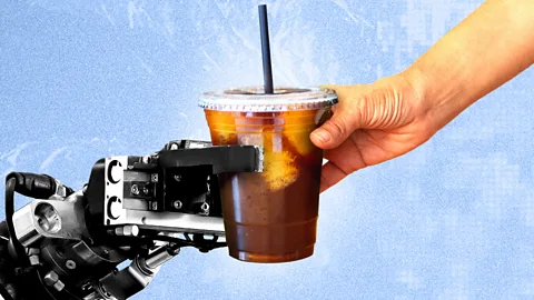 A robotic arm hands a cup of iced coffee with a straw to a human hand (Credit: BBC/ Serenity Strull)