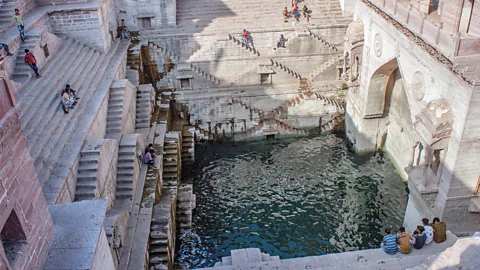 The restored Toorji Ki Jhalara stepwell, filled with water with people sitting around it on the steps (Credit: Alamy)