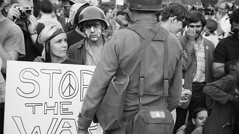 Protesters with placard reading 'Stop the war' and soldiers looking on