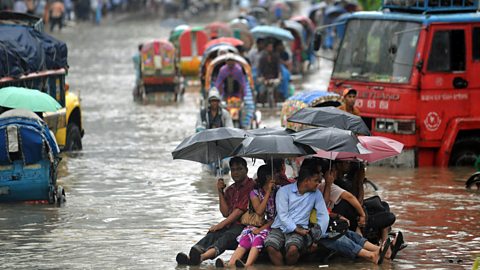 People attempt to stay dry over flood waters in the Bangladeshi capital of Dhaka
