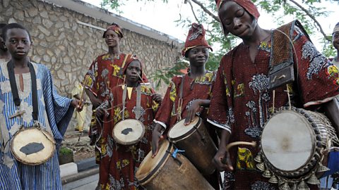 Drummers carrying their instruments dressed in traditional African dress.