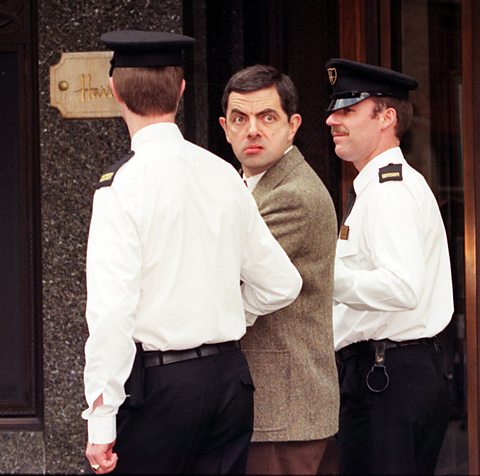 Rowan Atkinson yn chwarae rhan Mr Bean (1996) yn cael ei gludo gan ddau blismon