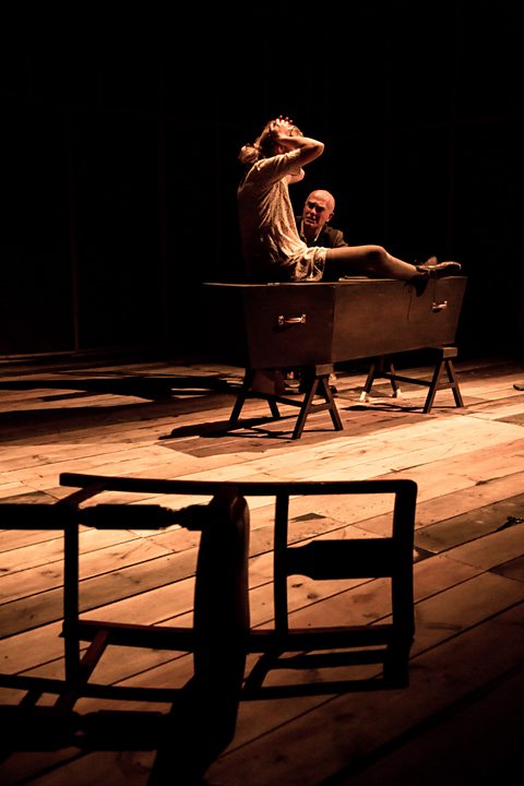 Dau actor ar lwyfan gyda chadair ar ei ochr ar lawr - perfformiad Rhwng Dau Fyd