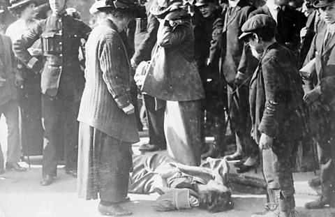 A suffragette lies on the ground as police and bystanders look on