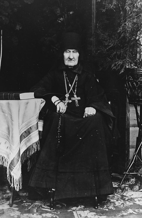 Black-robed man with two large crucifixes around neck