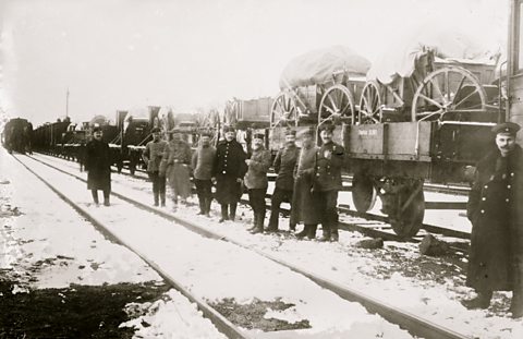 Smiling soldiers in front of railway wagons loaded with artillery pieces