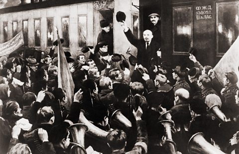 Lenin waves his hat in salute to gathered crowd as he steps down from a railway carriage