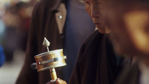 A Tibetan pilgrim in Lhasa using a prayer wheel.
