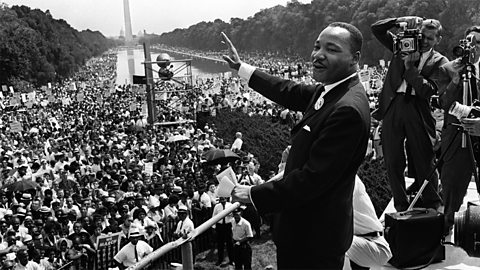 A black and white photograph of Martin Luther King delivering his ‘I have a dream speech’ at the March on Washington, in front of a large crowd of people.