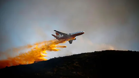 A DC-10 water bomber drops fire-fighting chemicals over a bush fire in San Marcos, California. Thousands of people near San Diego had to leave their homes due to fires. (Reuters)