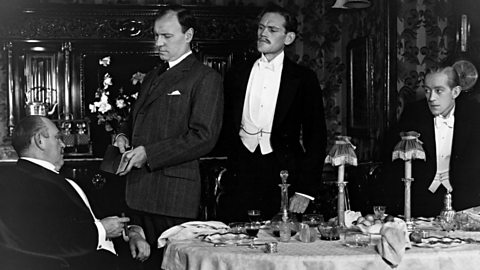 Photo from British premiere of An Inspector Calls. Inspector Goole interrogates Mr Birling with Eric and Gerald looking on (1946).