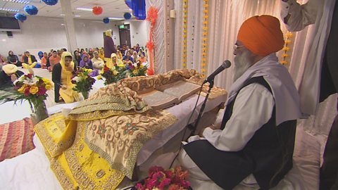 The religious leader with the Guru Granth Sahib as sikhs attend the gurdwara 