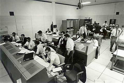 Mission control with lots of busy men in shirts and ties. 