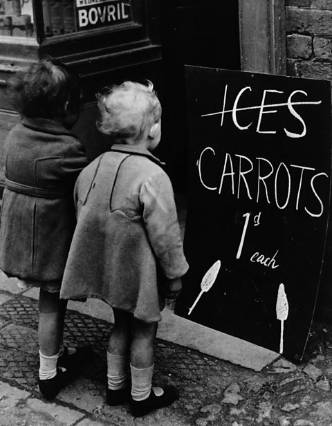 Two young children with a board advertising the enticing prospect of carrots on sticks in 1941.