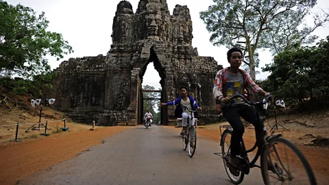 Christophe Archambault/Getty Cycling past the entry gates of Angkor Thom (Credit: Christophe Archambault/Getty)