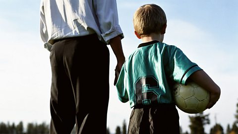 A photo of a young boy footballer, holding the hand of his father