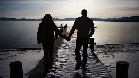 A couple holding hands on a pier of a lake