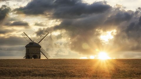 The autumnal sun setting on a corn field with a windmill