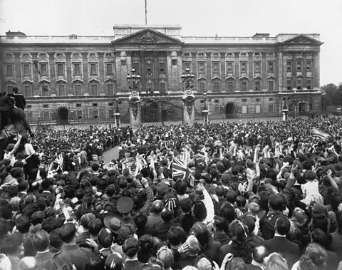 A black and white photograph of a crowd of people celebrating VE Day outside Buckingham Palace.