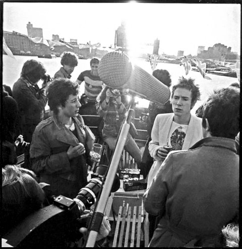 A black and white photograph of the Sex Pistols, with a microphone in the foreground of the image.