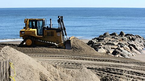 A bulldozer moves sand up the beach